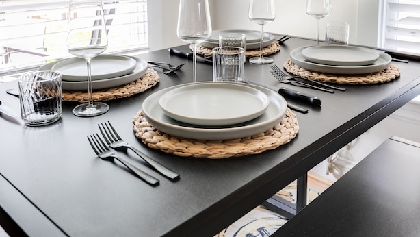 Een eettafel gedekt met borden, glazen en bestek, met geweven placemats en een donker tafelblad.