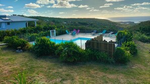 Un patio trasero con piscina, rodeado de abundante vegetación y vistas al océano.