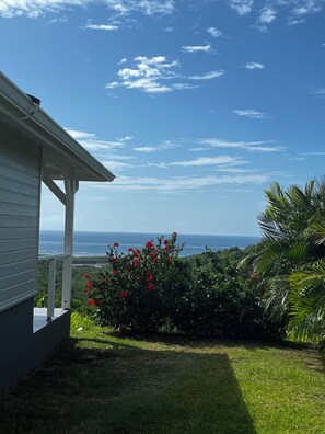 Ein Haus mit Blick auf den Ozean, ein Garten mit roten Blumen und ein klarer, blauer Himmel.