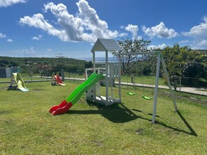 Un terrain de jeux avec des toboggans et des balançoires, entouré d’une clôture et de verdure.