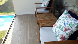Een balkon met een houten vloer, een bank met bloemenkussens en een houten tafel.