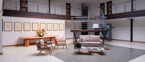 A spacious living area with a wooden bench, a sofa, and a coffee table. A staircase connects two levels, and there are framed pictures on the wall.