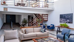 Un vaste espace de vie comprenant un canapé, une table basse et des fauteuils bleus. Un escalier avec une rampe en bois mène à l’étage supérieur.