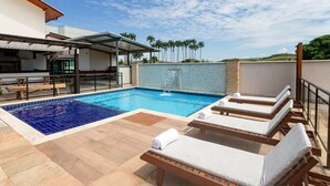 Un espace piscine avec des chaises longues, un coin salon abrité et une vue sur les palmiers.