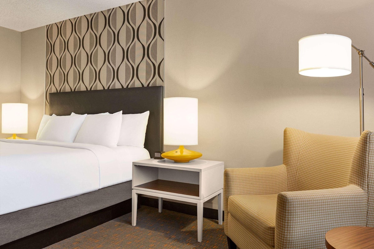 A hotel room with a bed, bedside tables, a lamp, a chair, and a patterned wall.