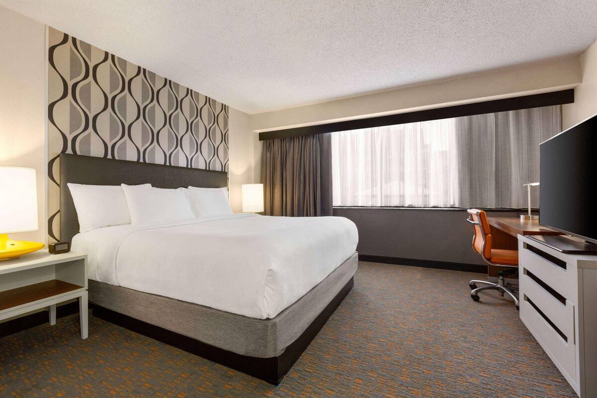 A hotel room with a large bed, a desk with a chair, a TV, and a window with curtains.