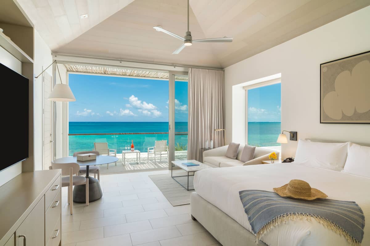 Een hotelkamer met een groot bed, een televisie, een balkon met uitzicht op de oceaan en een zithoek met een tafel en stoelen.