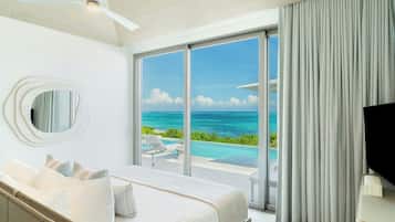 A bedroom with a bed, a ceiling fan, a large window with a view of the ocean, and a TV on a stand.
