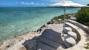 A clear view of the ocean with a wooden deck and a white umbrella. - Rock House (Providenciales)