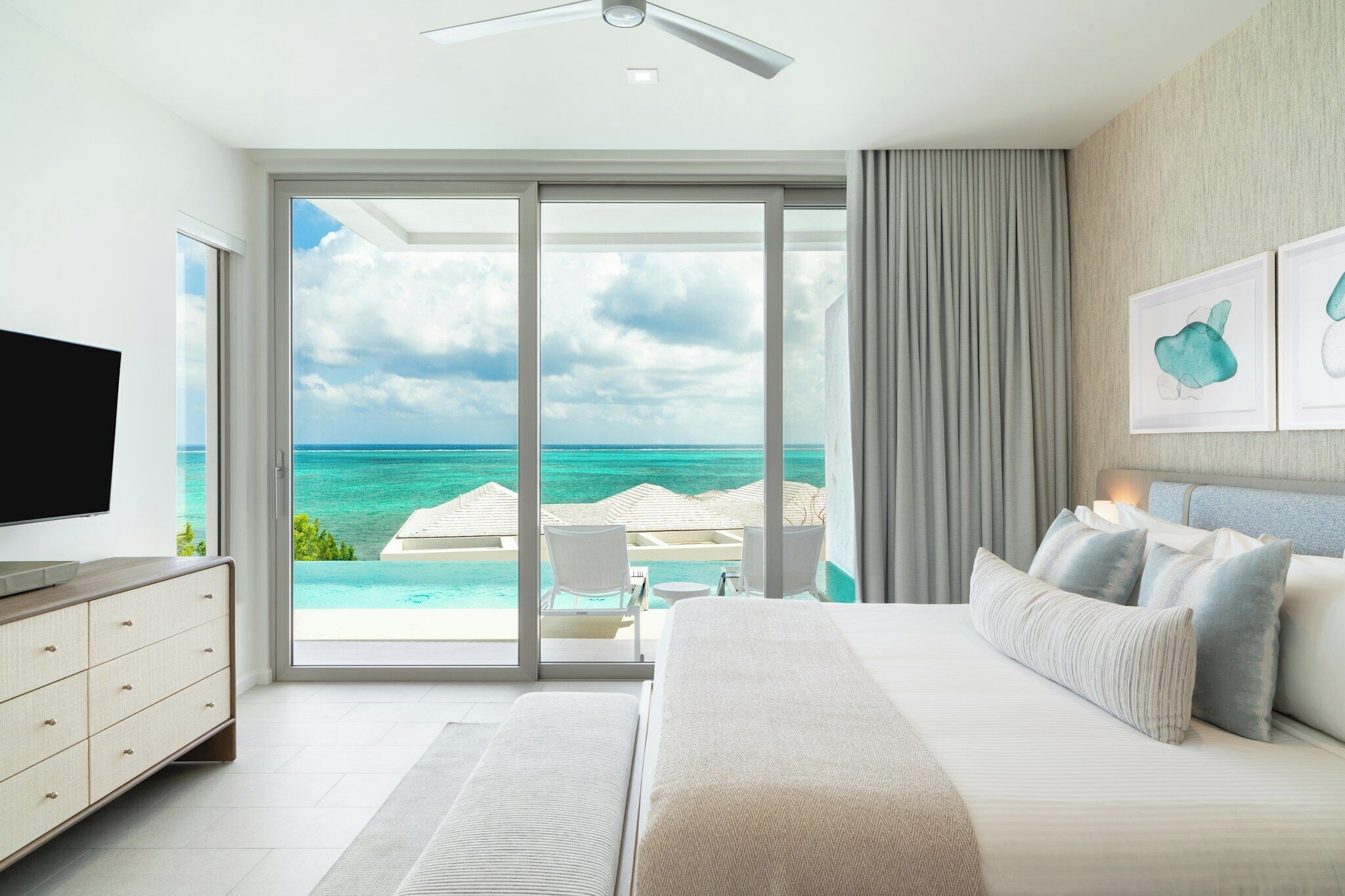 A bedroom with a large bed, a TV, and a view of the ocean through a sliding door.