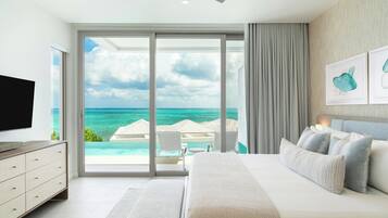 A bedroom with a large bed, a TV, and a view of the ocean through a sliding door.