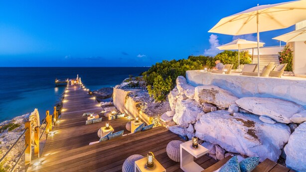 A wooden deck with outdoor seating and tables, overlooking a rocky coastline and the sea. - Rock House (Providenciales)