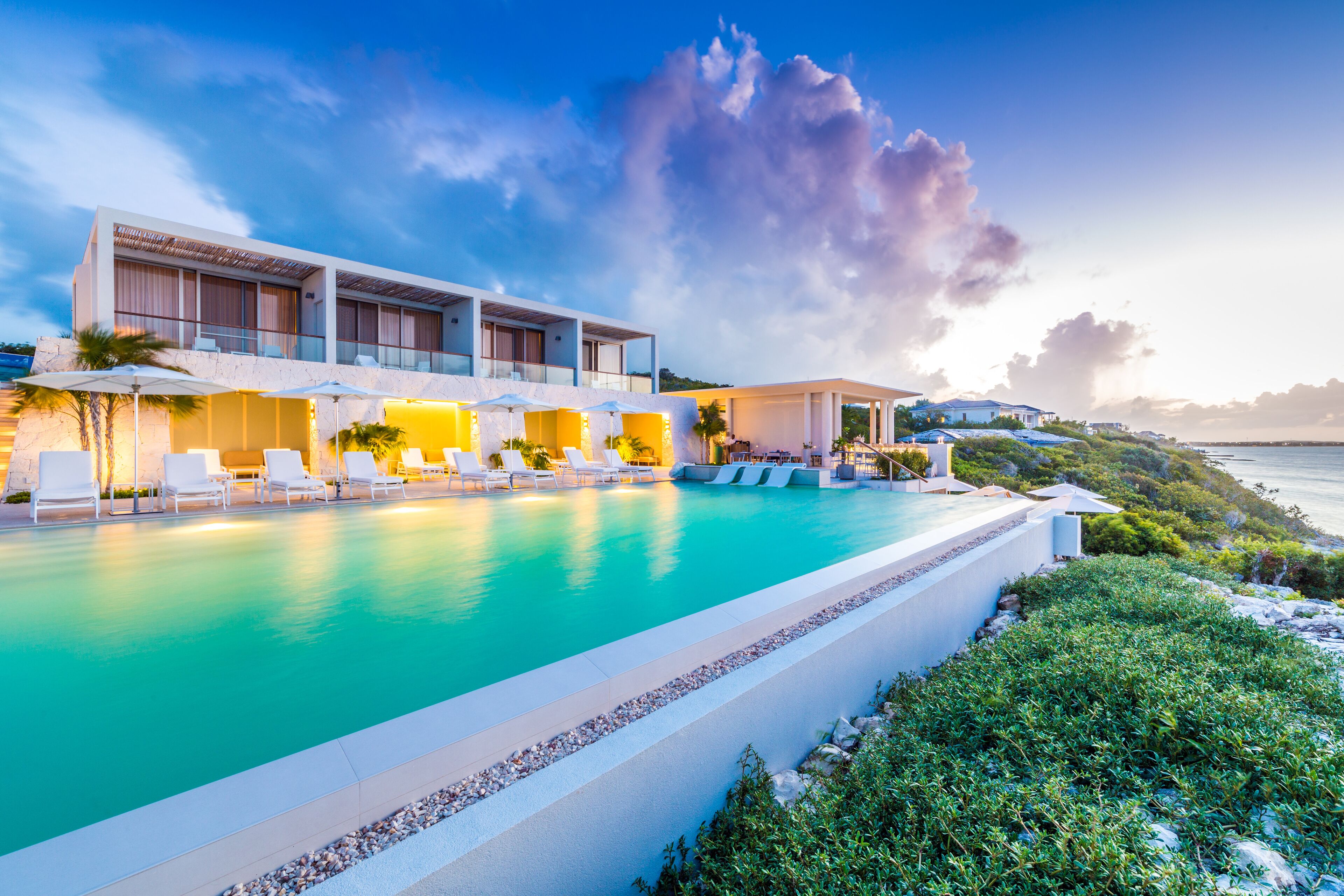A modern hotel with a pool, sun loungers, and a view of the sea.