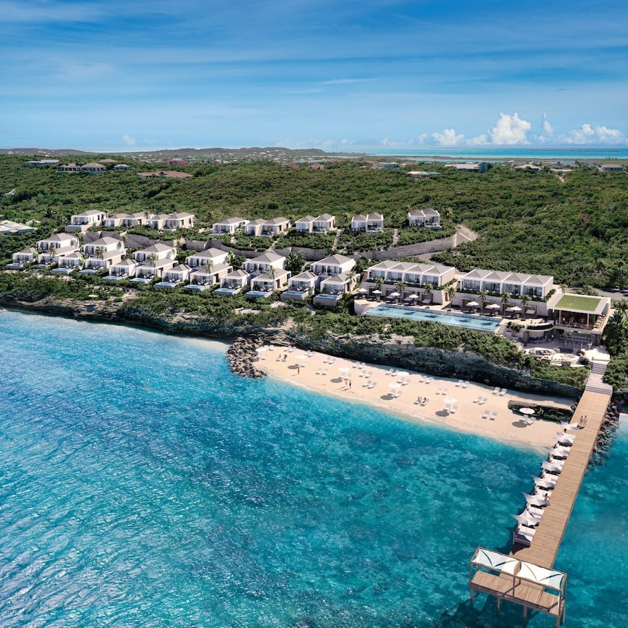An aerial view of a coastal resort with multiple bungalow-style accommodations, a central pool, and a beach area.