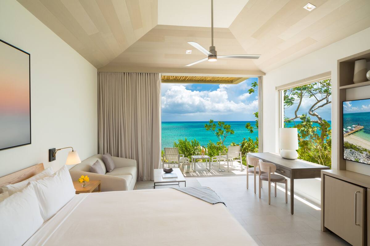 Een moderne hotelkamer met een bed, een bureau, een stoel en uitzicht op de oceaan.