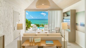 A modern room with a stone wall, a wooden table, a sofa, and a view of the ocean. - Rock House (Providenciales)