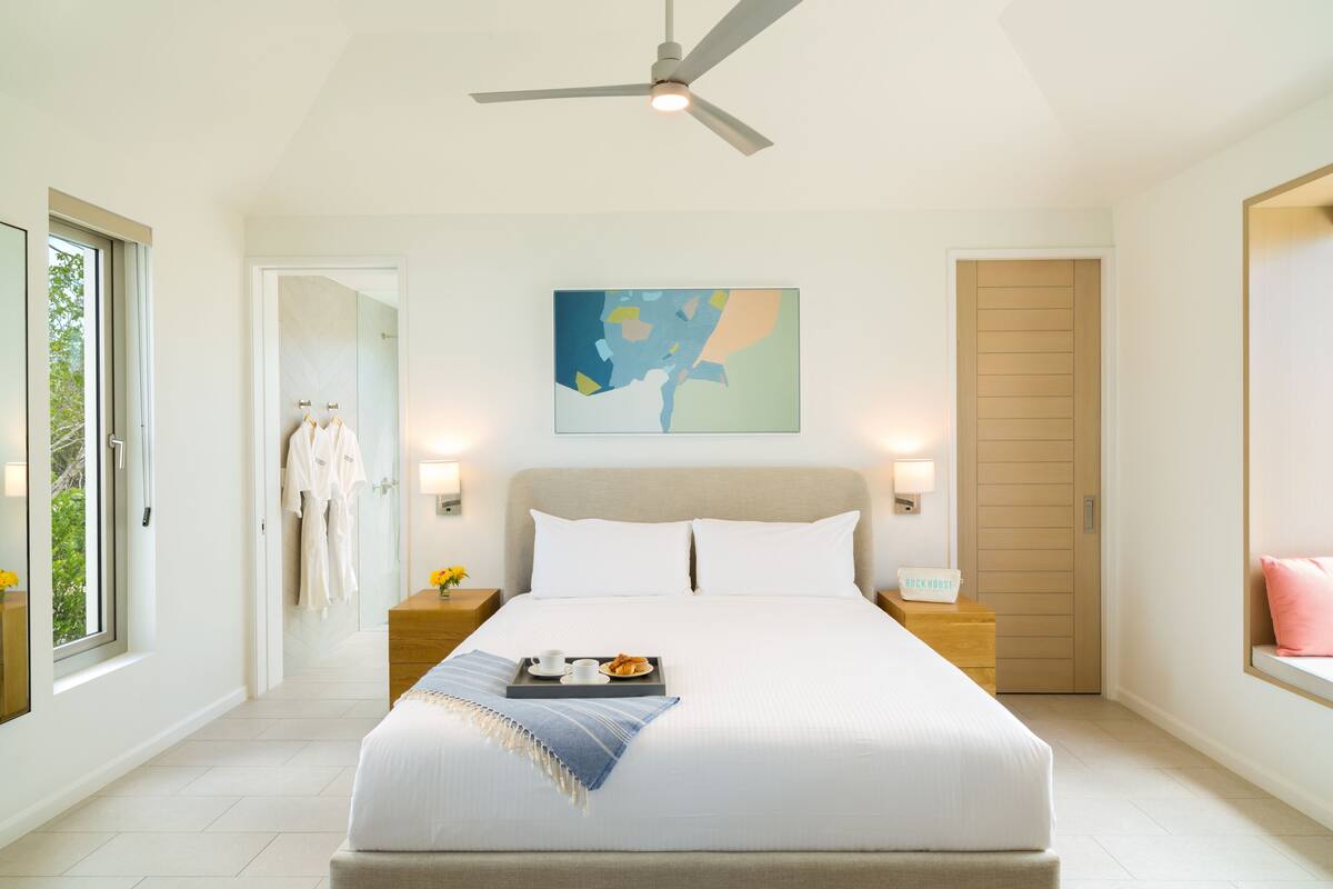 Een moderne slaapkamer met een groot bed, nachtlampjes, een plafondventilator en een raam met uitzicht.