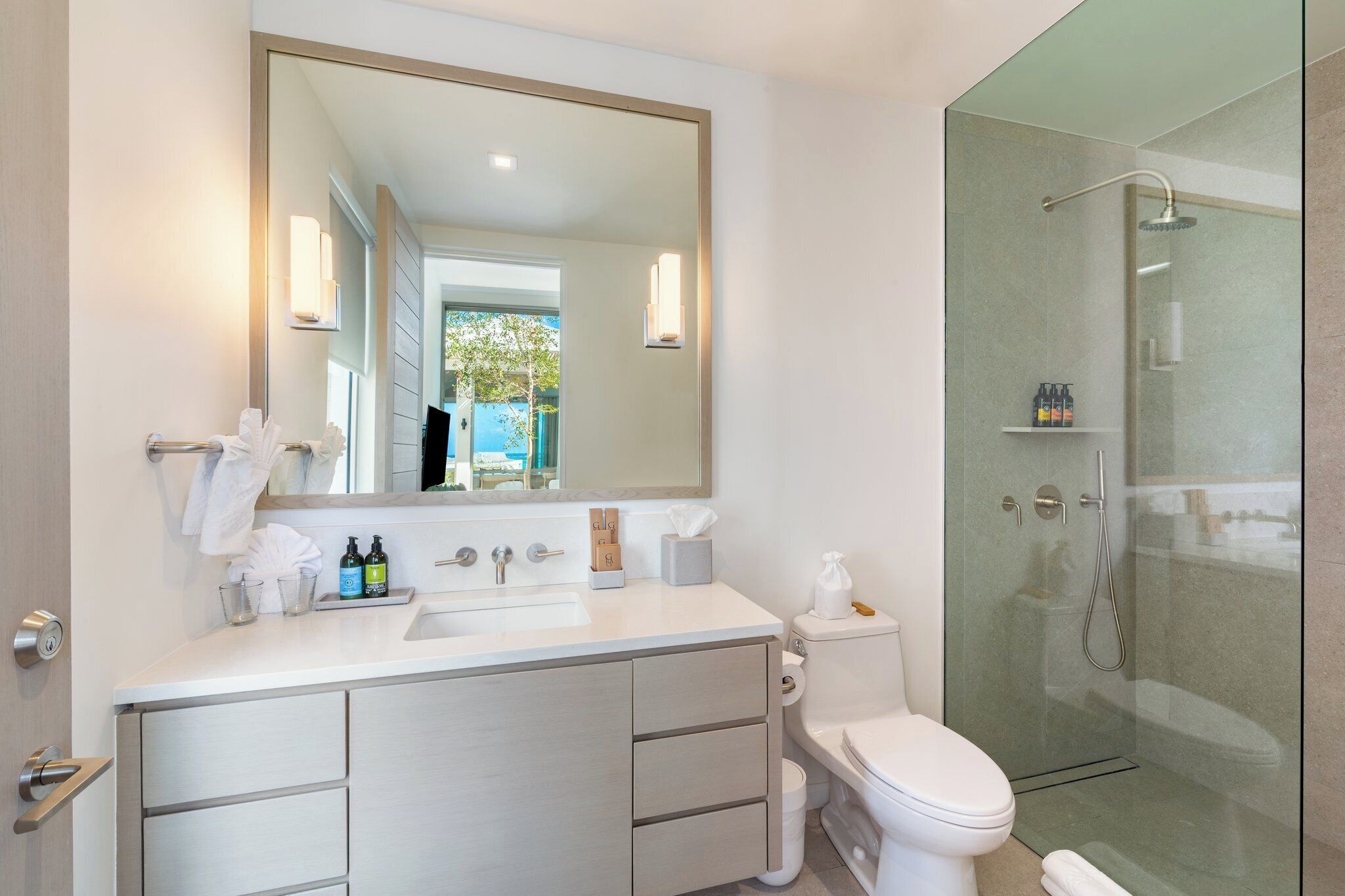A modern bathroom with a large mirror, a white sink, a toilet, and a glass-enclosed shower.