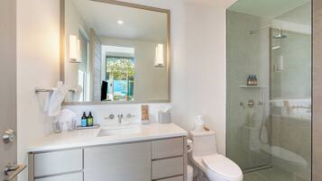 A modern bathroom with a large mirror, a white sink, a toilet, and a glass-enclosed shower.