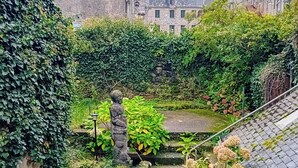 Eine Steintreppe führt zu einem Innenhof mit einer Statue, umgeben von üppigem Grün und historischen Gebäuden im Hintergrund.