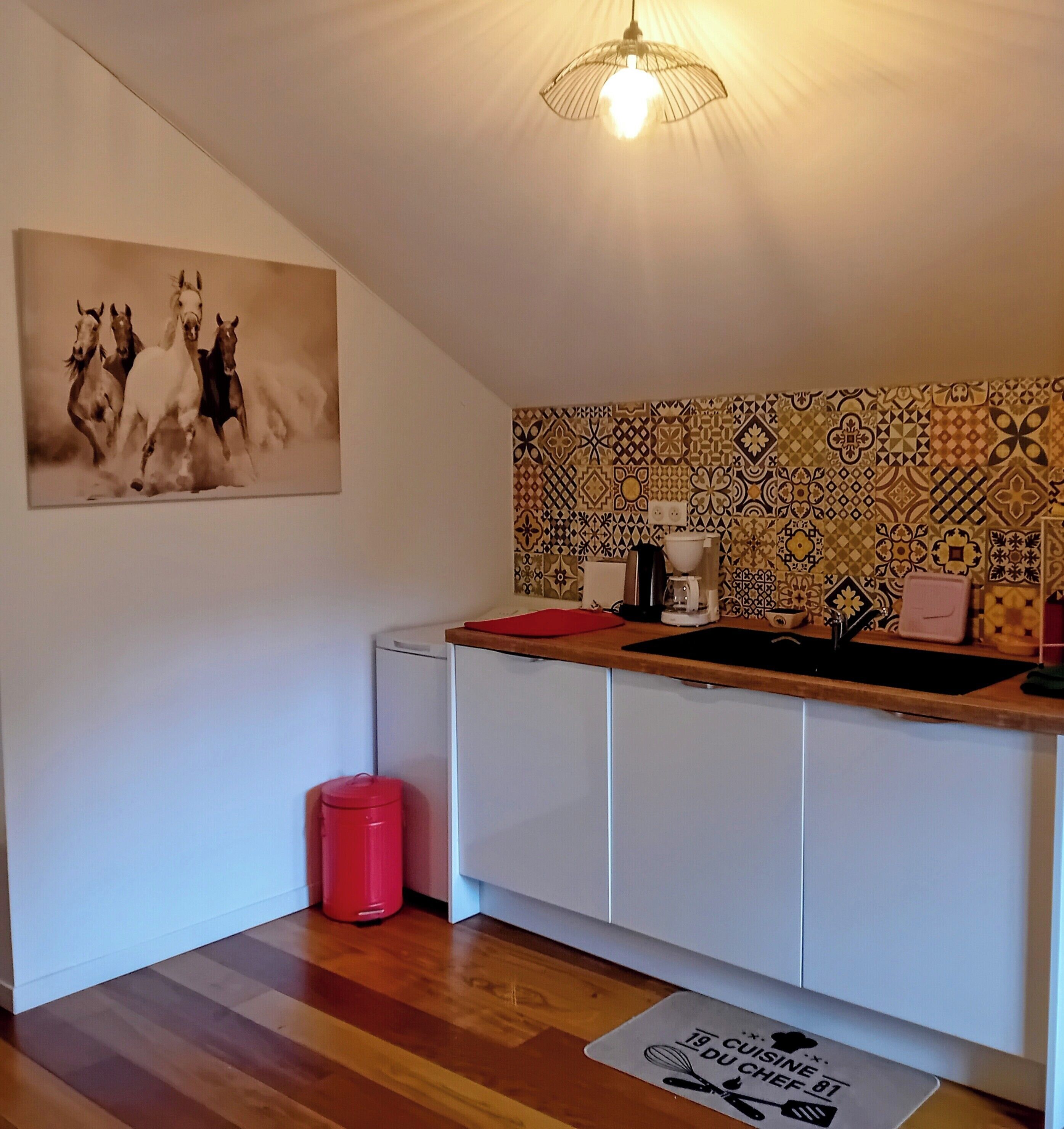 A kitchen with a patterned backsplash, a hanging light fixture, a red trash bin, and a placemat with text.