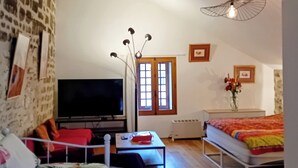 Ein gemütliches Wohnzimmer mit einer Couch, einem Fernseher, einem Couchtisch und einem Bett.