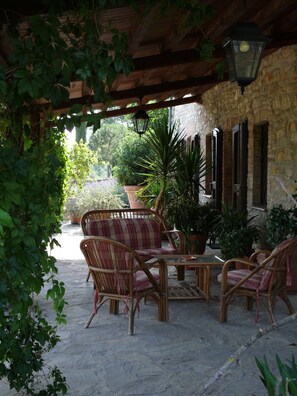 An outdoor patio with wicker furniture, a stone wall, and potted plants.