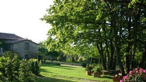A stone building with a tiled roof, surrounded by a well-maintained lawn and various potted plants.