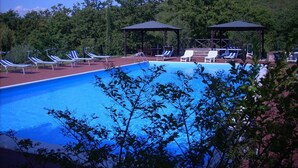 A swimming pool with lounge chairs and gazebos, surrounded by trees.