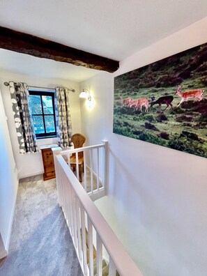 A staircase with a white railing, a window with patterned curtains, a desk with a lamp, and a wall with a wildlife painting. - Galtons Cottage Dorset (West Moors)