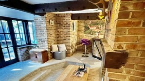A cozy room with exposed brick walls, a wooden table, a cushioned bench, and a small stool. - Galtons Cottage Dorset (West Moors)