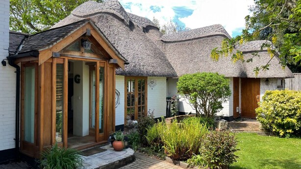 A traditional house with a thatched roof, wooden front door, and a small porch with potted plants. - Galtons Cottage Dorset (West Moors)