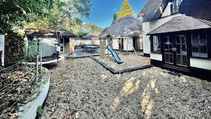 A courtyard with a play area, including a slide, surrounded by buildings with thatched roofs and large windows. - Galtons Cottage Dorset (West Moors)