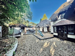 A courtyard with a play area, including a slide, surrounded by buildings with thatched roofs and large windows.