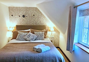 A bedroom with a large bed, two bedside lamps, a window with curtains, and a wall with a floral pattern.