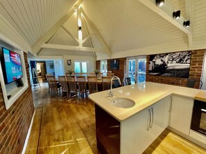 A spacious kitchen with a large island, wooden flooring, and a high ceiling with exposed beams. - Galtons Cottage Dorset (West Moors)