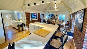 A spacious kitchen with a large island, wooden flooring, and a high ceiling with exposed beams. - Galtons Cottage Dorset (West Moors)