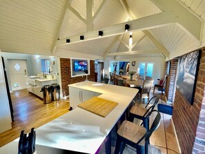 A spacious kitchen with a large island, wooden flooring, and a high ceiling with exposed beams.
