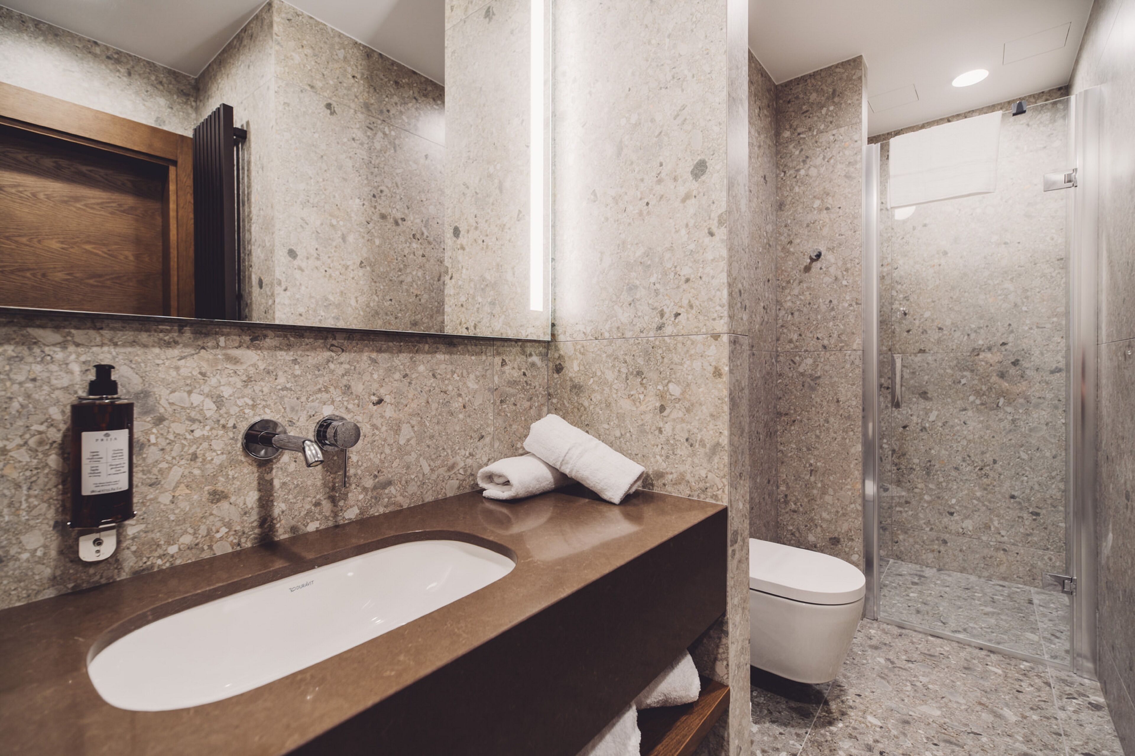 A modern bathroom with a marble sink, a mirror, a towel, and a shower area.