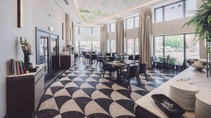 Un restaurant moderne doté d’un sol aux motifs géométriques, de grandes fenêtres et d’un plafond orné de motifs de feuilles.