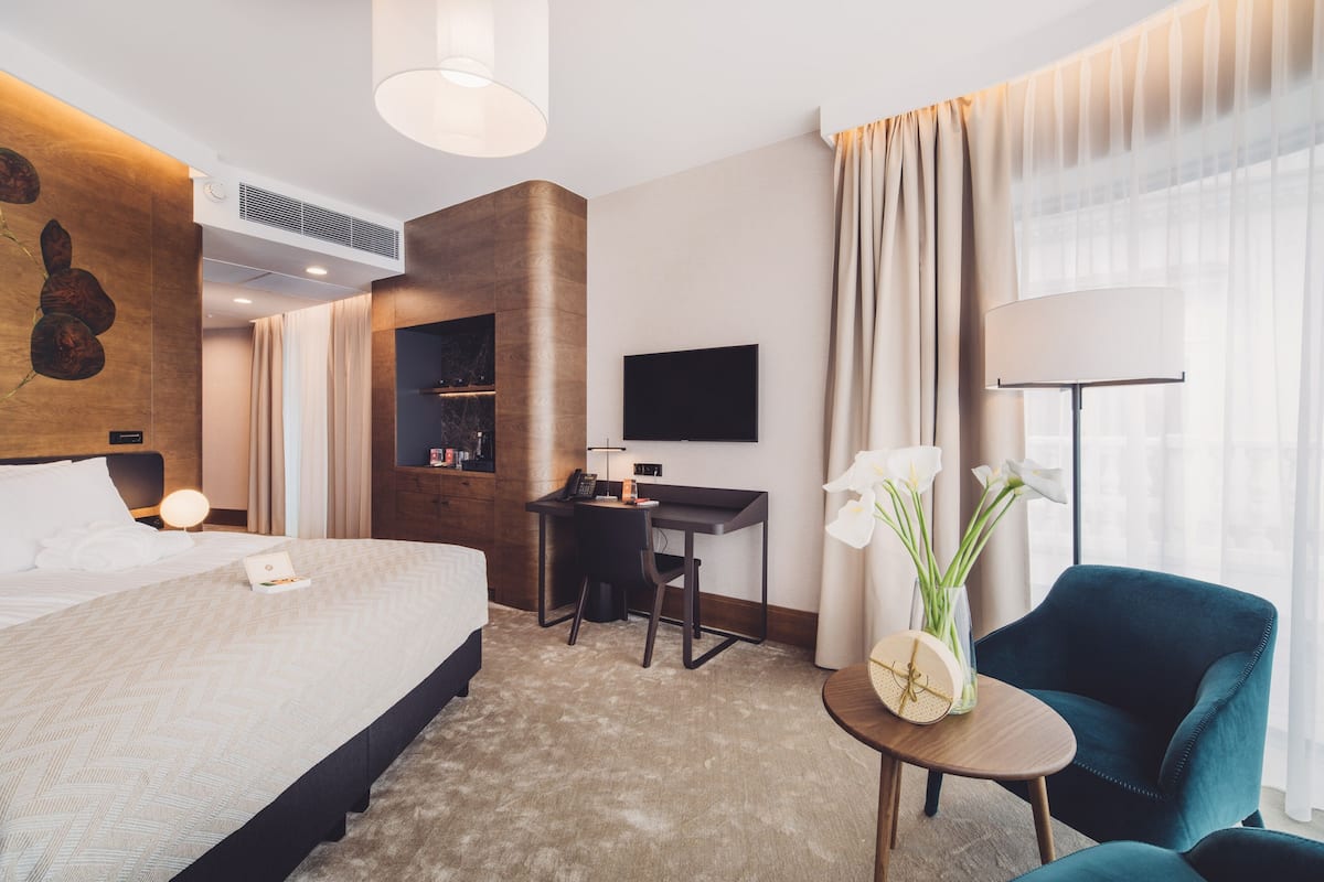 A hotel room with a large bed, a desk, a chair, a TV, and a lamp.