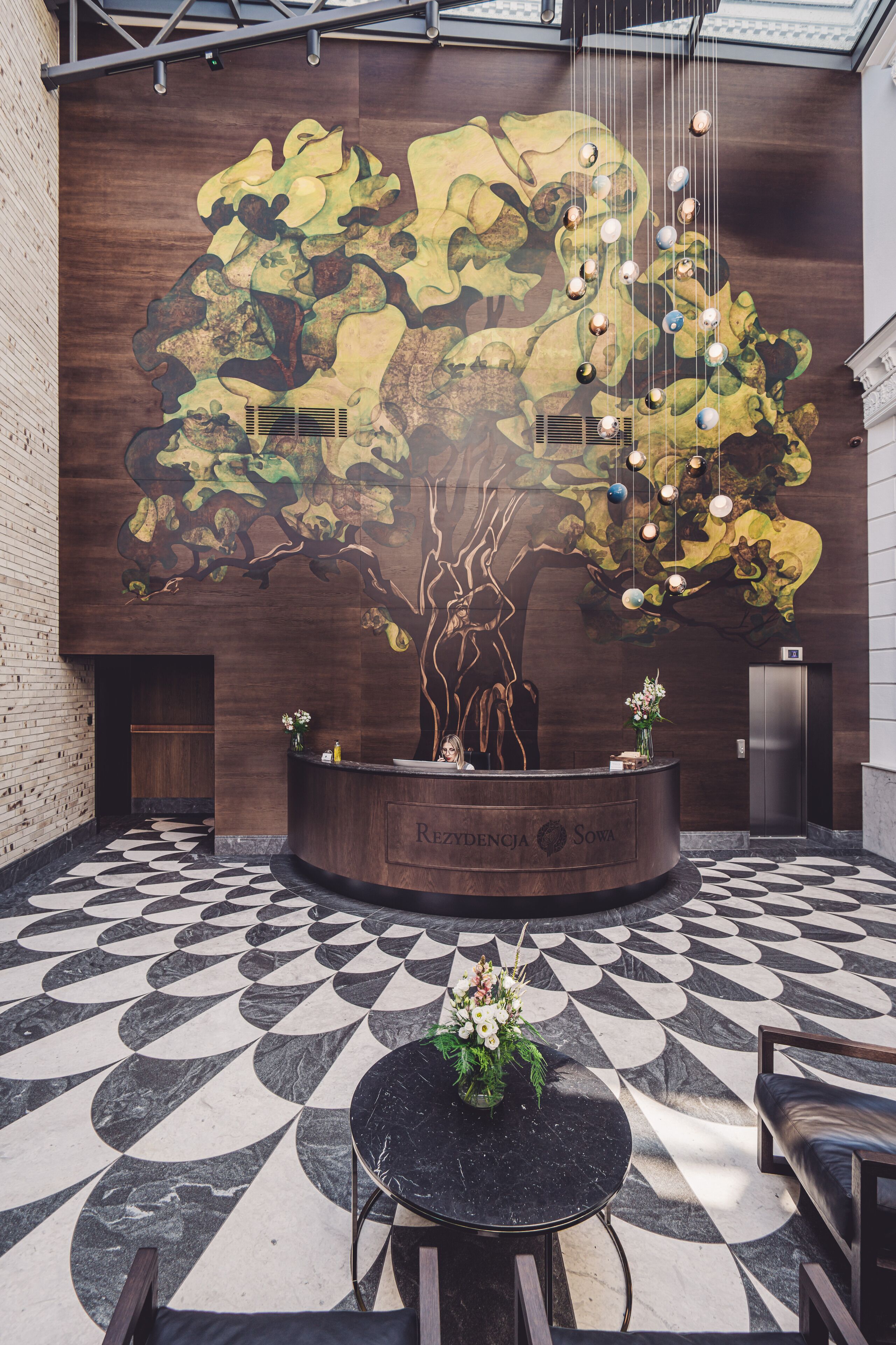 A lobby with a large mural of a tree, a reception desk, and a patterned floor.