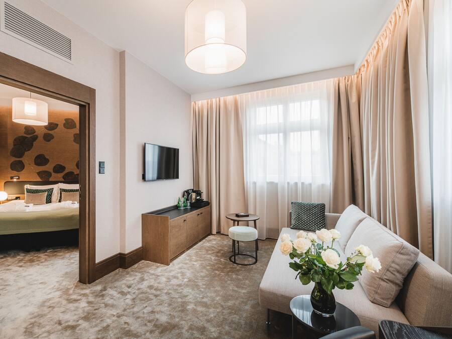 A hotel room with a bed, a sofa, a small table, a TV, and a window with curtains.