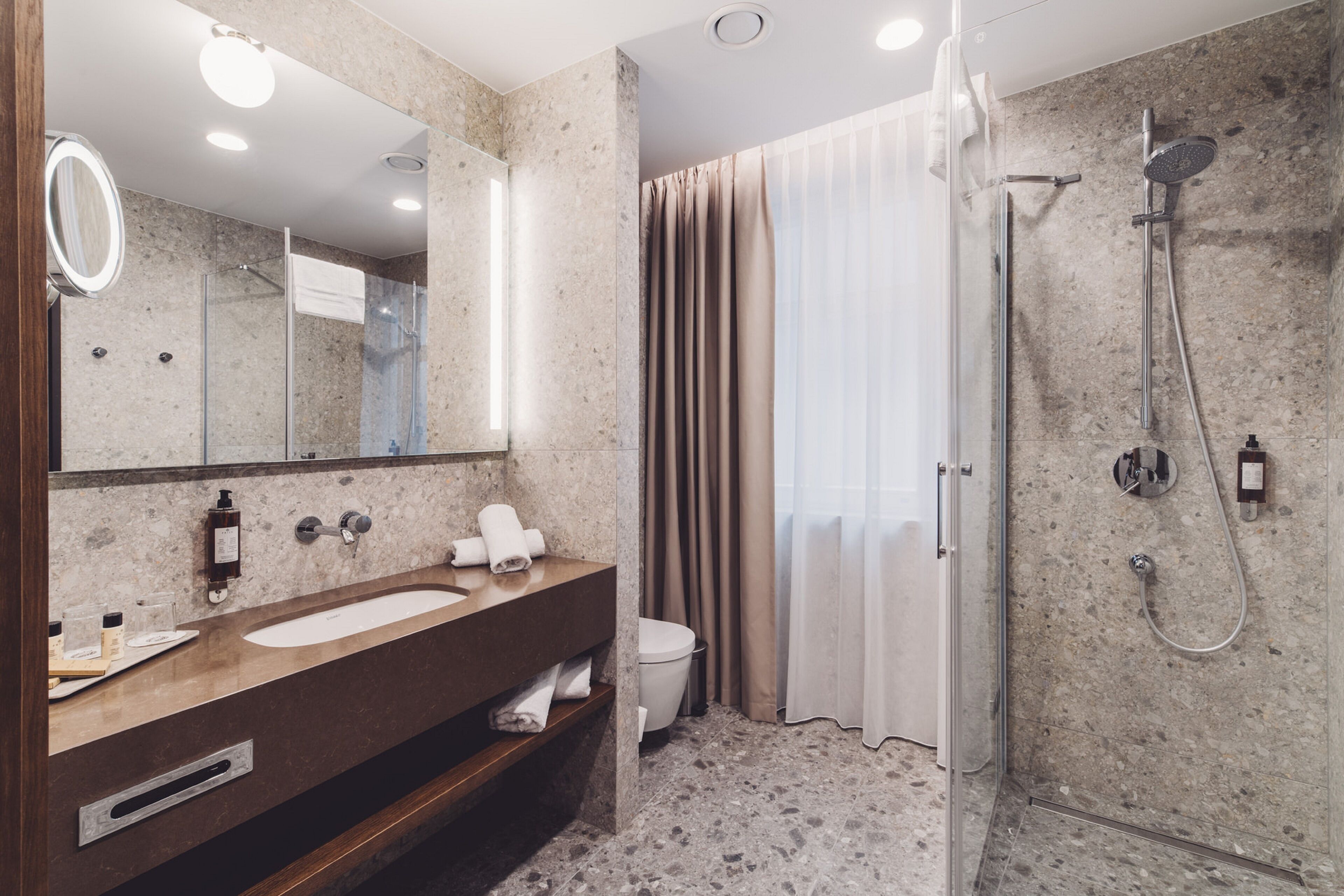 A modern bathroom with a marble sink, a glass shower enclosure, and a toilet.