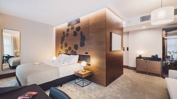 Una habitación de hotel moderna con una cama grande, una mesita de noche con lámpara, un escritorio pequeño con silla, una pared de acento de madera y un espejo amplio.