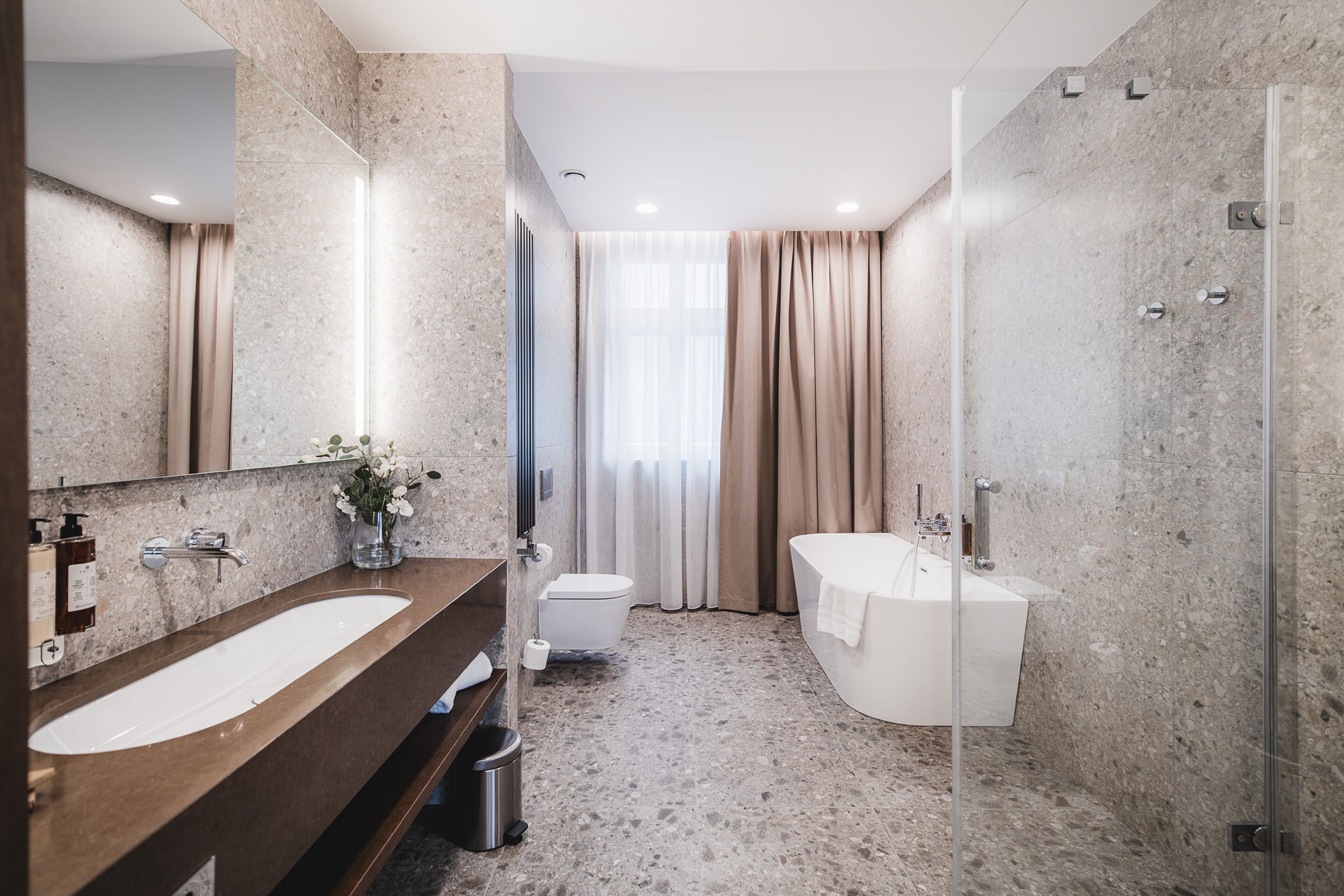 Een moderne badkamer met een marmeren wastafel, een badkuip en een douche met glazen wanden.