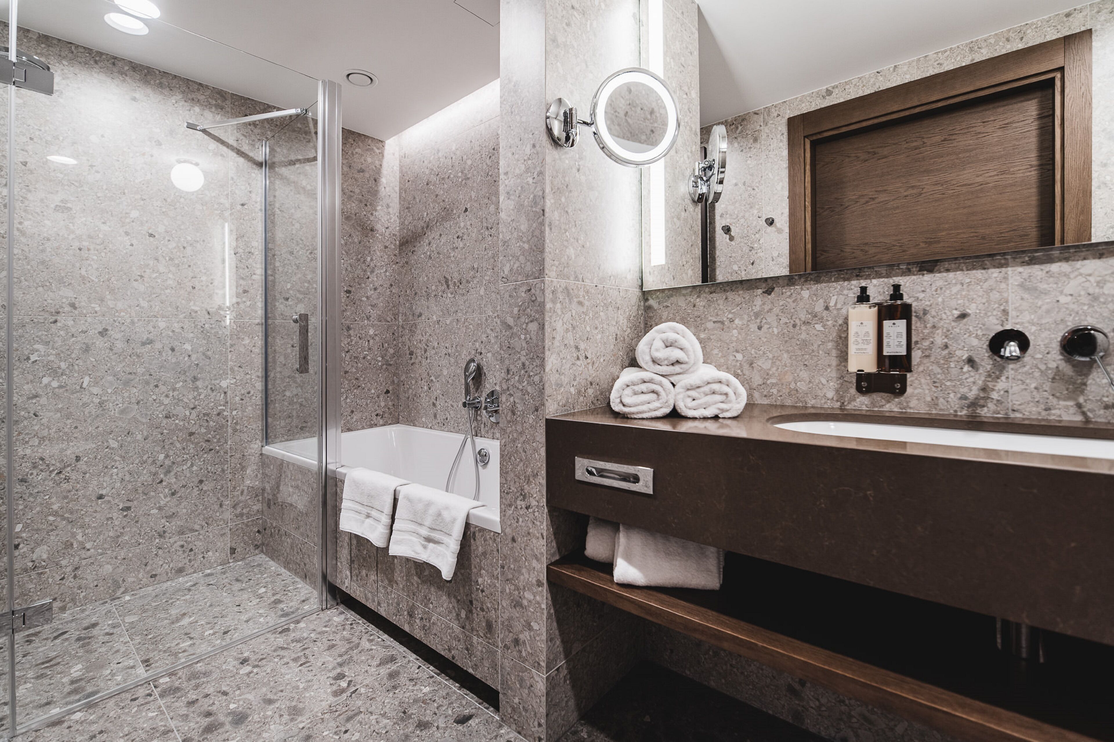Ein modernes Badezimmer mit einer gläsernen Duschkabine, einer Badewanne und einem Waschtisch mit Spiegel und Pflegeprodukten.