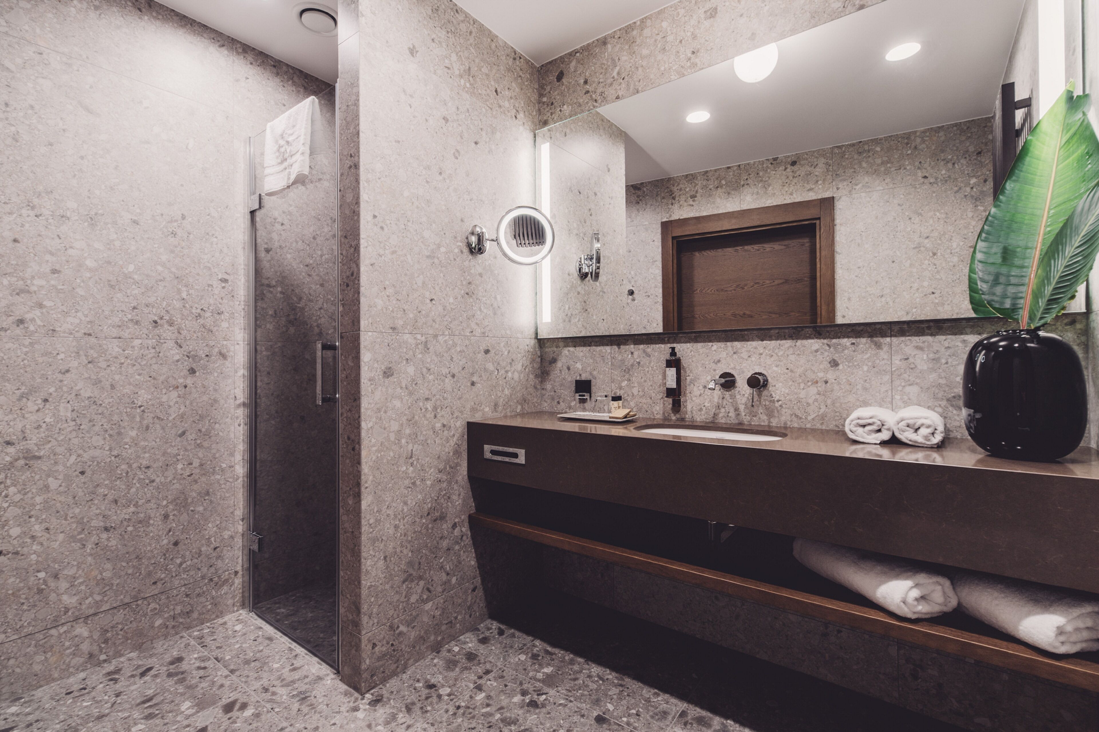 Un baño moderno con encimera de granito, cabina de ducha de vidrio y un espejo grande.