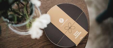 Una mesa redonda de madera con una caja etiquetada “Czech story Czełoklady” y un jarrón con flores blancas.