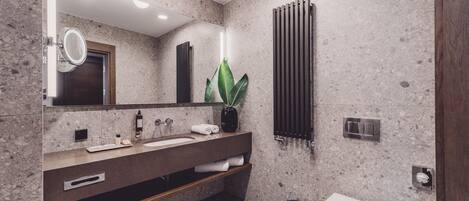 A modern bathroom with a granite countertop, a large mirror, a potted plant, a towel rack, and a toilet.